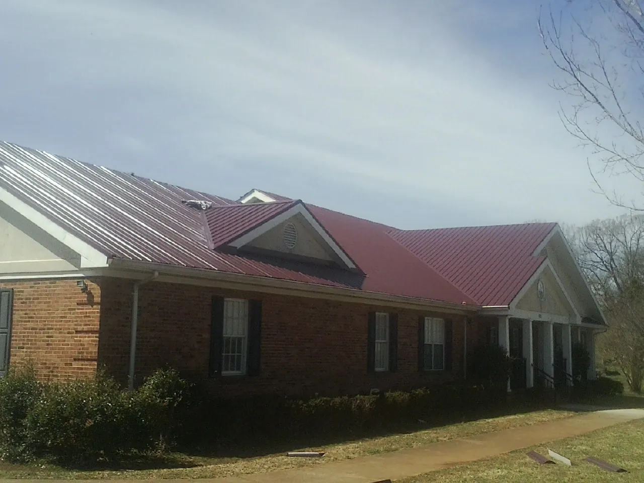 Red metal roof with gabled entries on a long brick building, from a Hail Damage Roof Repair job in Benton
