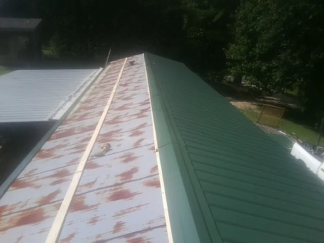 Old rusted panels beside newly installed green metal roofing — Wind Damage Roof Repair by Roofing Brothers in Benton