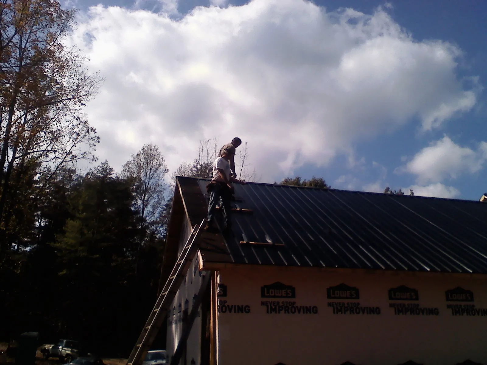 Roofer fastening dark metal panels high against a cloudy sky, from a Roof Inspection job in Benton